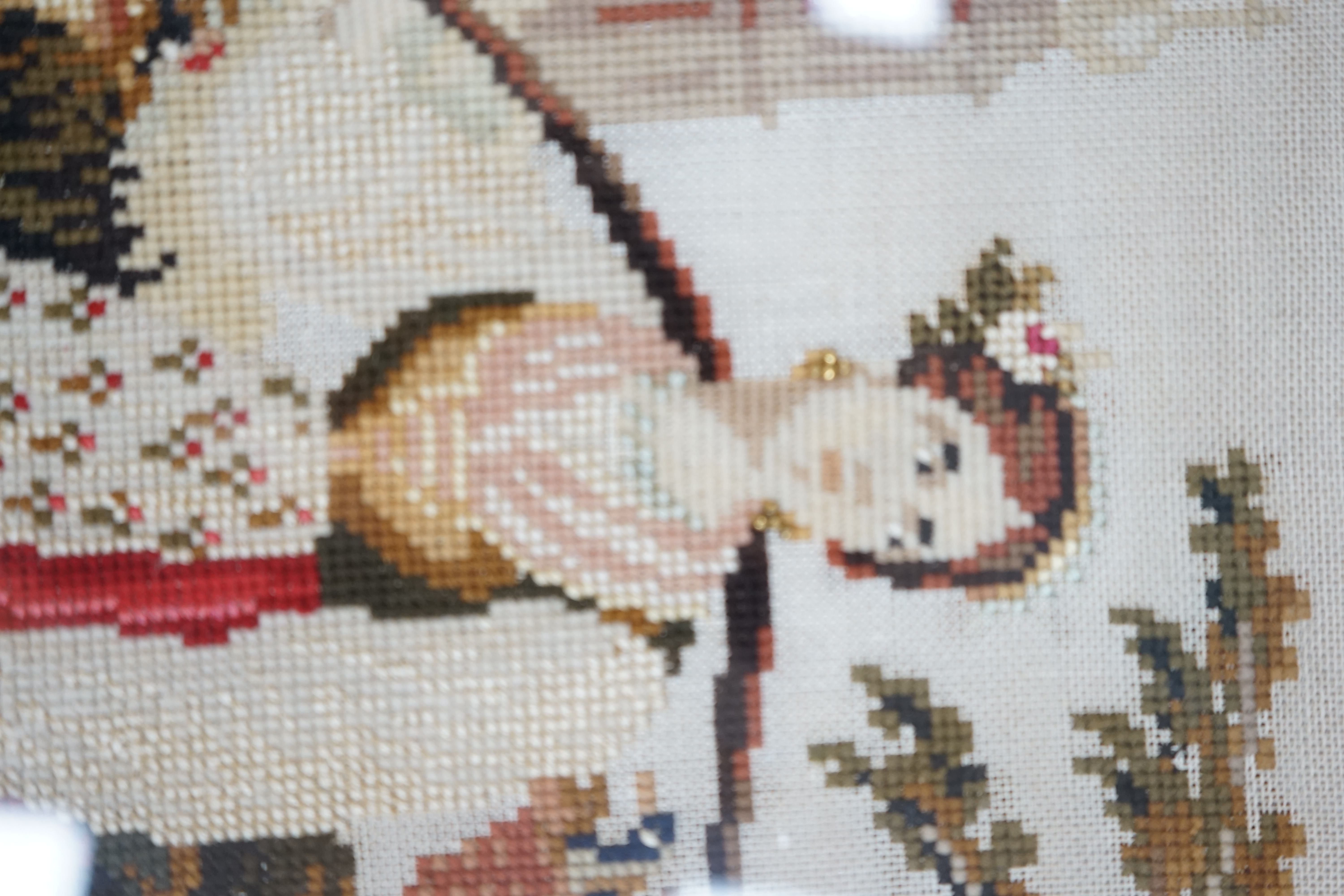 A framed 19th century Berlin wool worked embroidery of a peasant girl carrying panniers by a church, with the steeple in the background, 30cm x 38cm